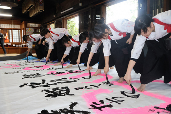 曲に合わせて筆を走らせる豊川高書道部員ら＝岡崎市真福寺町の真福寺で