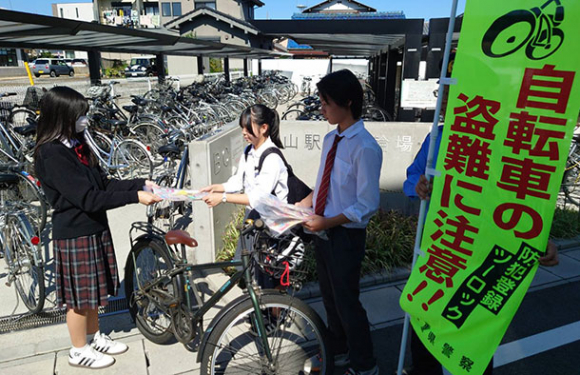 亀山駅の駐輪場で、利用者にチラシなどを配る高校生（左）ら＝亀山市で