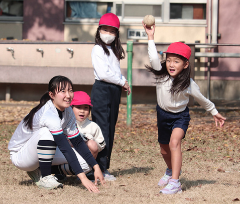ボールを投げる児童を見守る生徒（左）＝東区の東桜小で