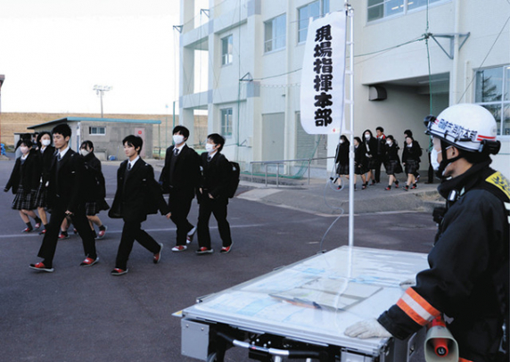 消防隊員（右）の指示でグラウンドへ避難する生徒ら＝岡崎市中園町の岡崎城西高で