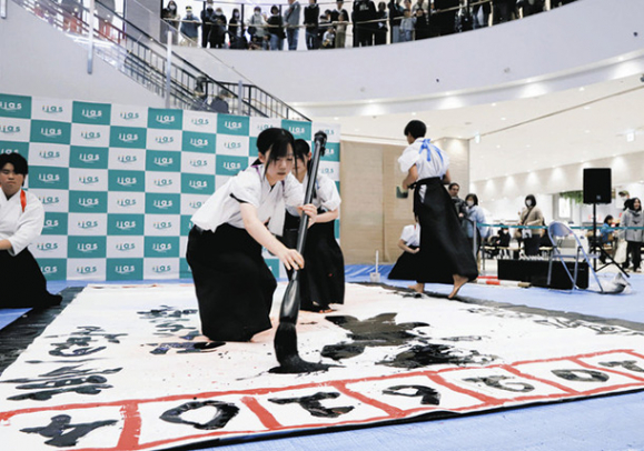 巨大な紙に筆を走らせる中部大春日丘高の書道部員＝春日井市六軒屋町のイーアス春日井で