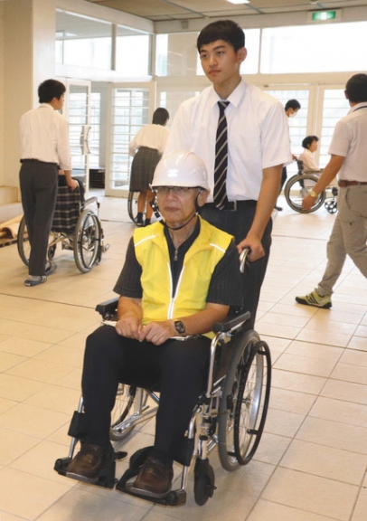 車いすに乗って生徒に避難誘導される住民ら＝津市一身田の高田中・高で