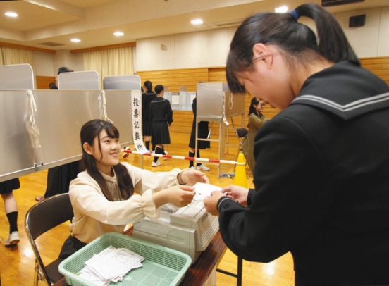 模擬投票で、学生から投票用紙を受け取る高校生（右）＝瑞穂区汐路町４で
