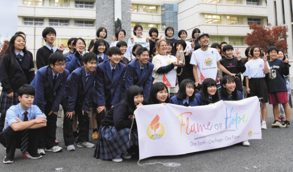希望の火を囲み、記念撮影する桜丘高の生徒とNPO法人アースキャラバンのメンバー=豊橋市南牛川の桜丘高で