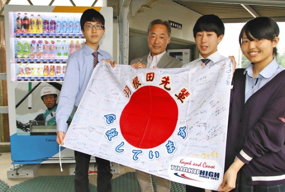 寄せ書きを持つ羽根田邦彦さん(左から2人目)と生徒たち。左奥は羽根田選手の写真がラッピングされた応援自動販売機=豊田市平戸橋町の杜若高で