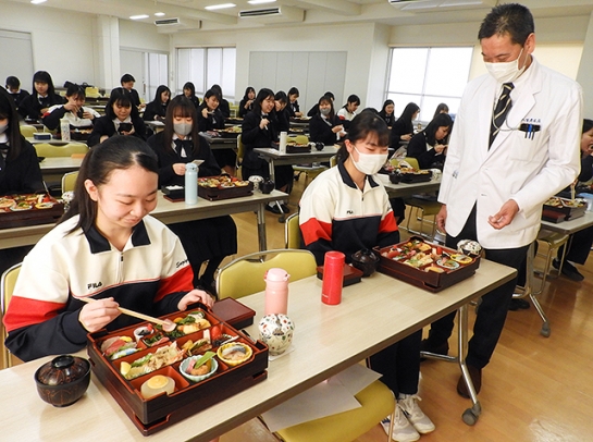 戸田取締役（右）の説明を受け、食育を考えた特製の割子弁当を味わう生徒たち＝千種区山添町２の椙山女学園高で