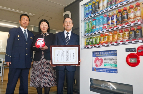 寄付型自販機設置の感謝状贈呈式に出席した（右から）三輪常務、小島委員長、千種署の河野清仁署長＝千種区若水３の愛知工業大名電中で