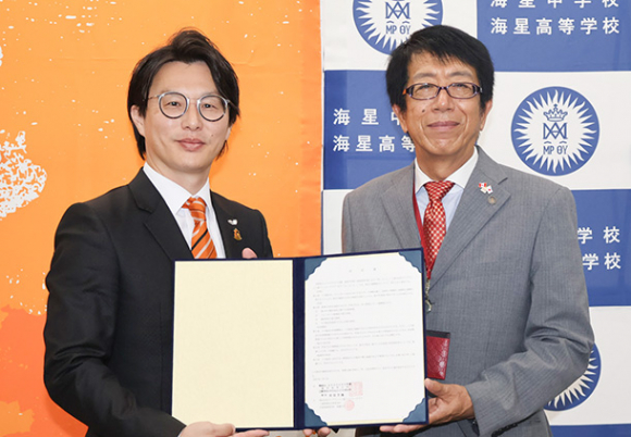 協定書を手にする椎葉常務（左）と服部校長＝四日市市追分の海星中学・高校で