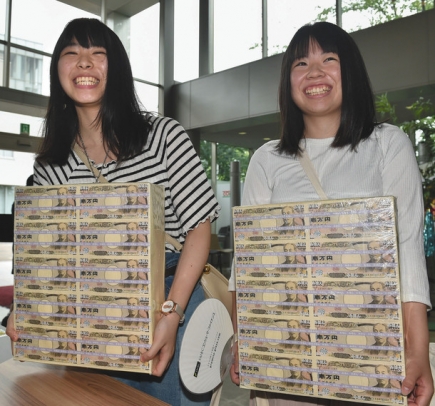 １億円分の模造紙幣の束を抱える高校生＝千種区の椙山女学園大で