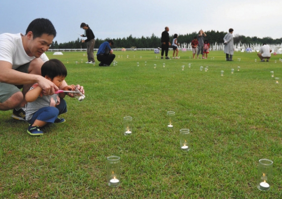 芝生広場に並んだキャンドルに点火する来場者ら＝能登町上町の柳田植物公園で