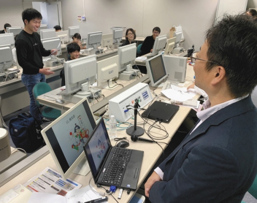 金栄部長（手前右）からアドバイスを受け、「桃太郎」を記事風にまとめる学生ら＝春日井市松本町の中部大で