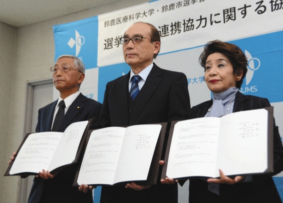 署名した協定書を掲げる（左から）今井委員長、豊田学長、高木委員長＝鈴鹿市の鈴鹿医療科学大で