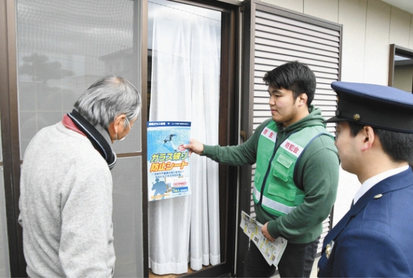 家人にガラス割り防止シートを貼るなど対策を促すティーギャップスの土江さん(左から2人目)=豊田市汐見町で