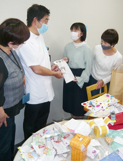 長江院長（左から２人目）にメッセージとプレゼントを贈る三井さん（右から２人目）と朝倉教授（右）＝緑区の南生協病院で