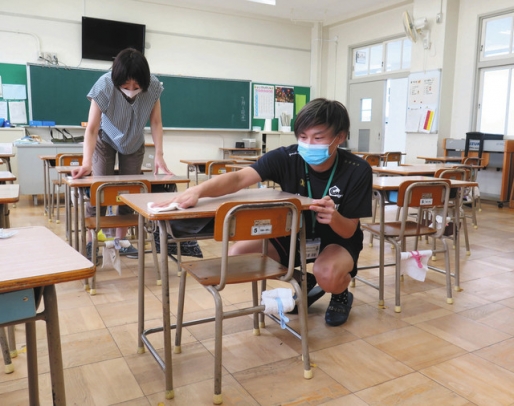 教員と一緒に机を消毒する愛知東邦大の氏原さん＝名東区の引山小で