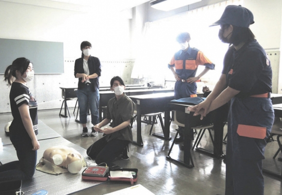 胸骨圧迫の方法を学生消防団員に指導する榎さん（右）＝四日市市萱生町の四日市大で
