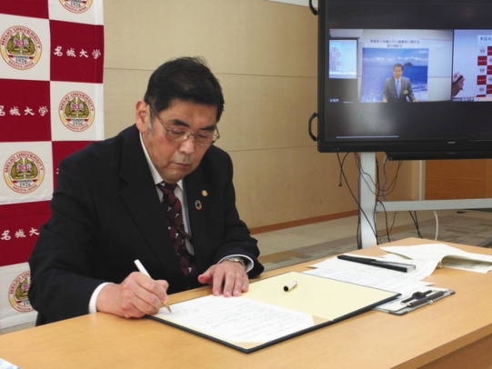 オンラインの締結式で、協定書に署名する小原学長（奥の画面は林市長）＝天白区の名城大で