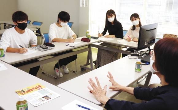 伊藤代表（右）の話を聞く中京大の学生たち＝亀山市東町の市民協働センター「みらい」で