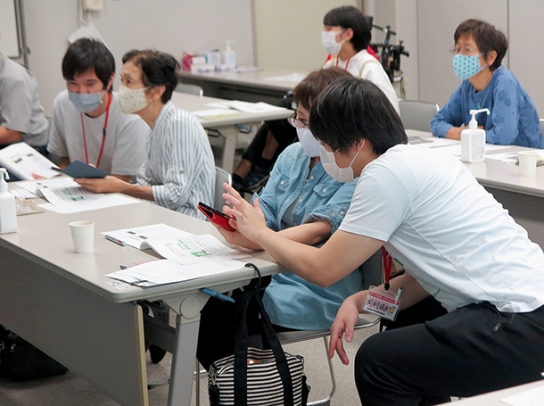 参加者にスマホの使い方を教える学生ら＝武豊町の思いやりセンターで（町社会福祉協議会提供）