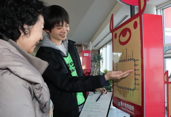 バスの利用者（左）に試作したバス停型端末を紹介する学生＝野々市市役所で