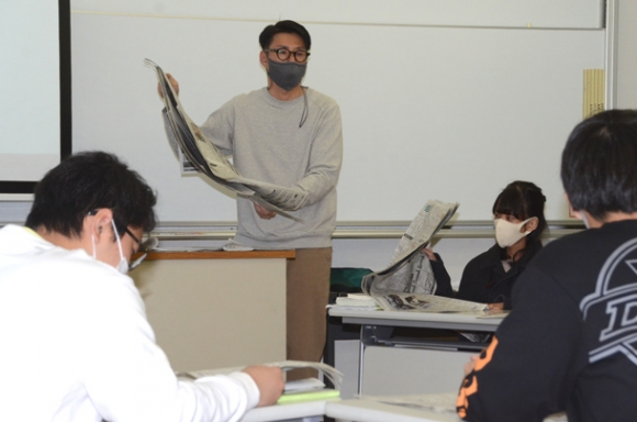 学生らに新聞の紙面や役割を紹介する村主さん（中央）＝鈴鹿市の鈴鹿大で