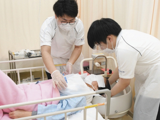 患者役を演じた現役看護師の髪を洗う学生たち＝一宮市の修文大で