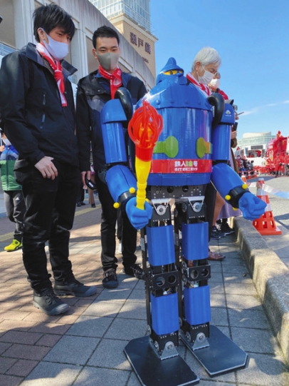 歩道から聖火リレーを応援する鉄人１８号と岩崎さん（左）、服部さん（中）、古橋教授（右）ら＝瀬戸市蔵所町で
