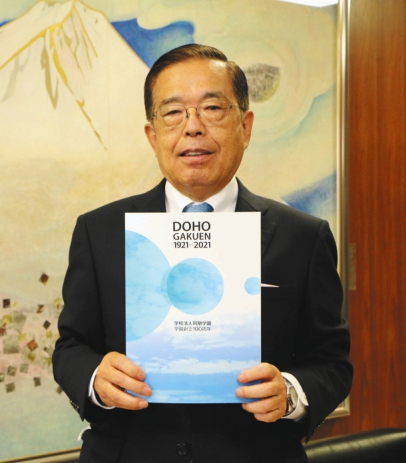 学園の創立１００年記念誌を手にする甲村理事長＝名古屋市中村区の同朋学園で