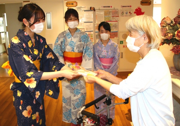 入所者（右）に暑中見舞いのポストカードを手渡す学生たち＝稲沢市大塚北９のケアハウス信竜で