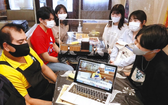 インド料理店のアローラさん（左）に完成したビデオを見せる中京大の学生たち＝港区七番町４のデリーパレスで