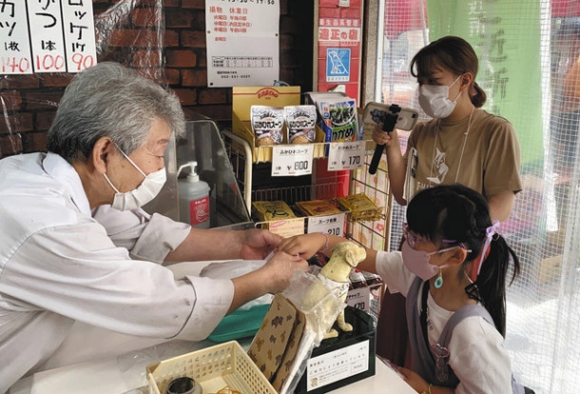 精肉店で目当てのコロッケなどを購入する女児＝西区の円頓寺商店街で