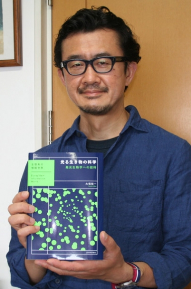 著書を手に「発光生物の研究を以前のように盛り上げたい」と話す大場教授＝春日井市の中部大で