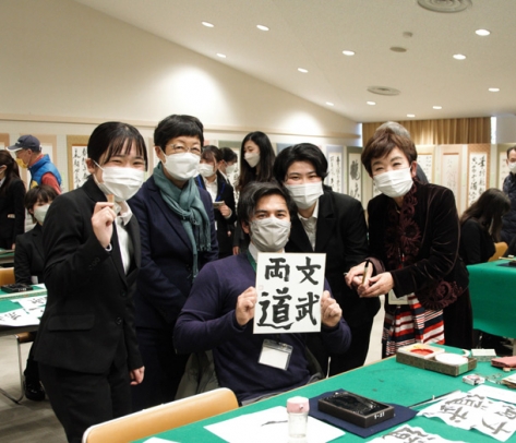 書道の体験をする県の国際交流員（前列中）と、手ほどきをする岐阜女子大の学生ら＝岐阜市美江寺町の市民会館で