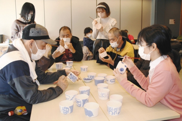 学食で使う磁器に絵付けする学生と障害者ら＝北区山田２のソーネおおぞねで