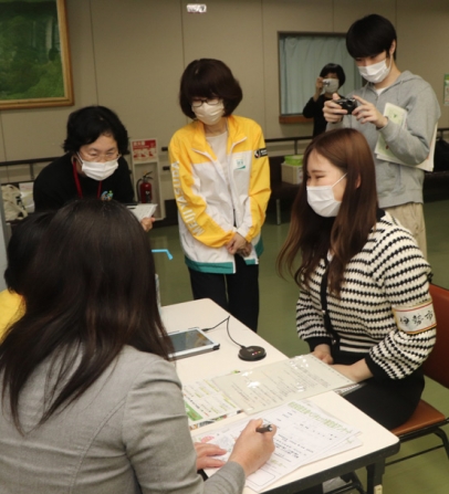 野菜摂取量の計測を体験する学生（右）と撮影する学生（右奥）＝伊勢市健康福祉センターで