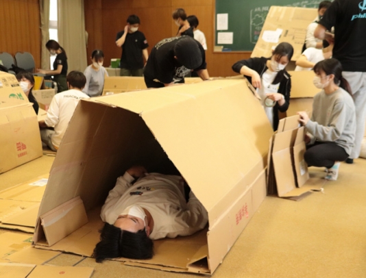 段ボールシェルターの寝心地を確かめる学生ら=美浜町の美浜自然の家で