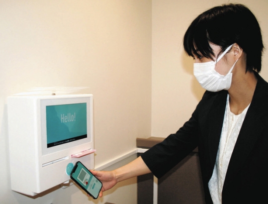 装置にスマホで取得したアプリをかざし、ナプキンを取り出す実演をする担当職員=熱田区の名古屋学院大で