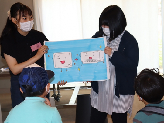 児童らにプラスチック製のトレーの再利用後の用途を伝える大学生ら＝長久手市勝入塚のリニモテラス公益施設で