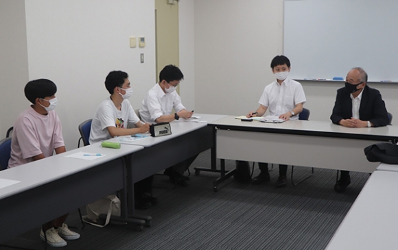 上島さん（右）から事業の説明を受ける学生ら＝伊勢市神田久志本町の皇学館大で