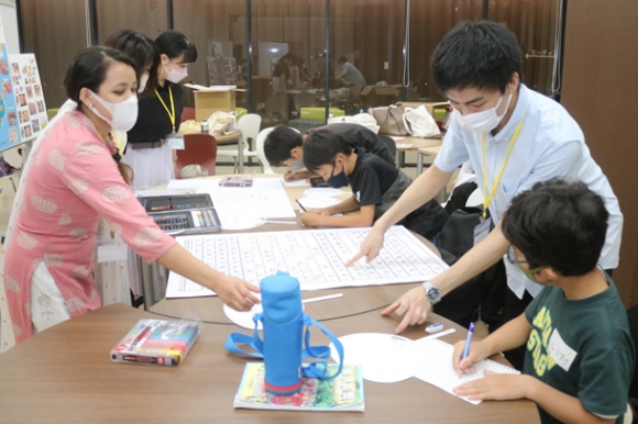 ネパール出身のカドカさん（左）に教わりながら、デーバナーガリー文字でうちわに自分の名前を書く児童ら＝東海市芸術劇場で