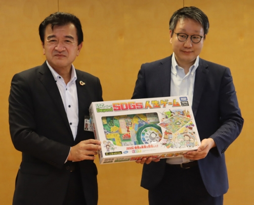 開発したＳＤＧｓを学べる人生ゲームを粟貴章市長（左）に手渡す平本督太郎所長＝野々市市役所で