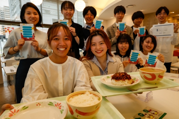 自分で皿に丼をひっくり返して完成させる尾張中村めしをＰＲする学生たち＝中村区平池町の愛知大で