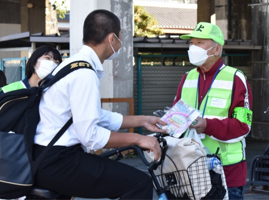 ワイヤ錠などの啓発物を学生に渡す参加者＝伊勢市の近鉄宇治山田駅近くで