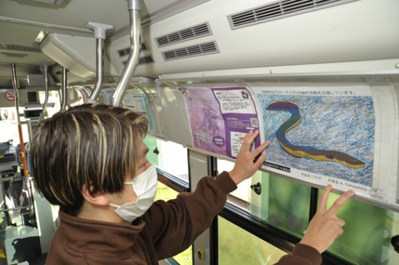 出発前のバス車内で山下さんの作品を掲示する関さん＝大府市のＪＲ大府駅東口ロータリーで