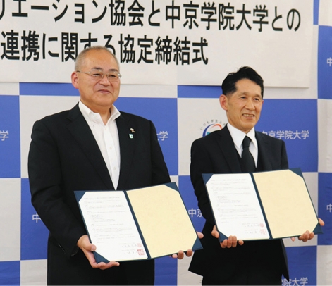 サインを交わした調印書を掲げる渡辺会長(左)と林学長=瑞浪市土岐町の中京学院大瑞浪キャンパスで