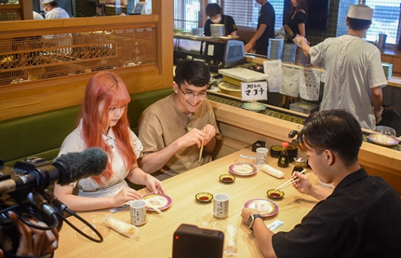 ＰＲ動画の撮影ですしを味わう（左から）謝さん、ラヒモフさん、遠山さん＝南知多町豊浜の回転まるはで