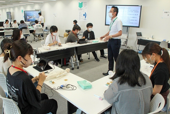 きゅうの効果などについて説明を受ける参加者たち＝鈴鹿市南玉垣町の鈴鹿医療科学大白子キャンパスで