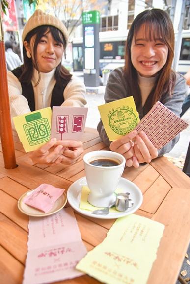 バス停を改良したテラス型の停留場で、利用客にコースターを提供する学生たち＝中区錦３で