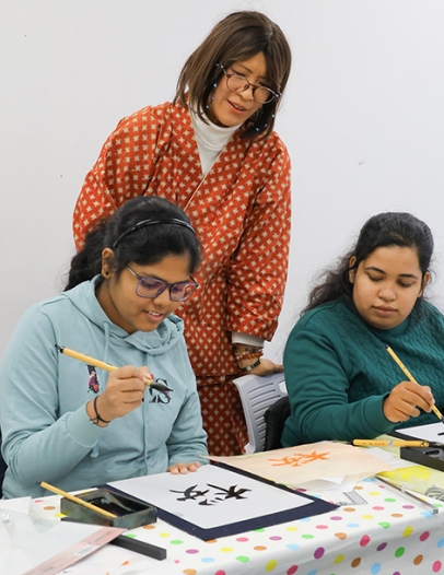インド出身の留学生に書道を教える里映さん（中）＝天白区の名城大で