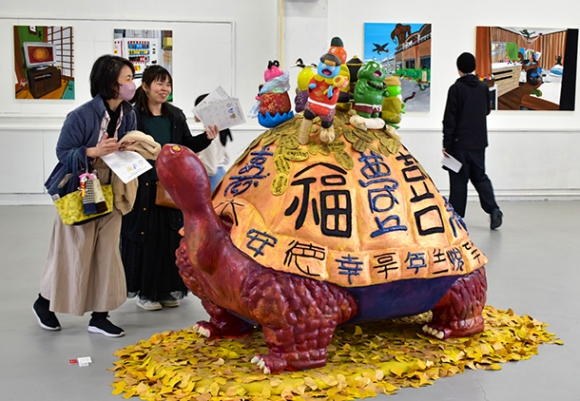 七福神を背負った作品「七福亀」に笑みを浮かべる来場者＝北名古屋市徳重西沼の名古屋芸術大西キャンパスで